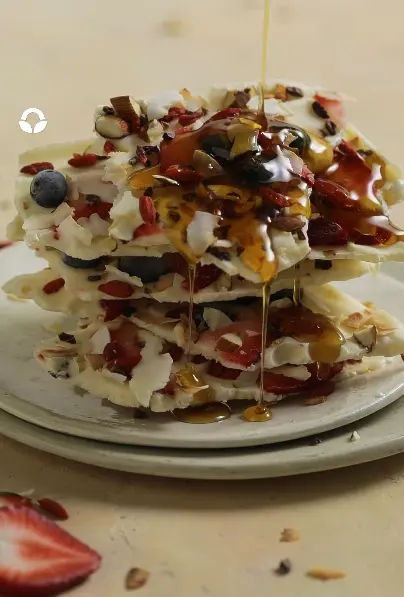 Pink blended berry yogurt bark pieces topped with strawberries, blueberries, raspberries, granola, and almonds