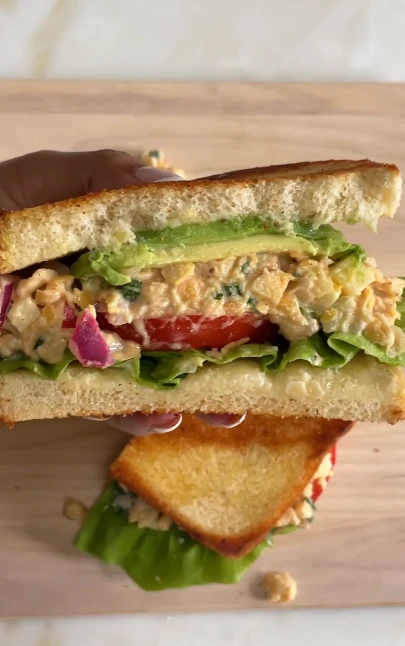 Vegan chickpea salad sandwich on toasted bread with lettuce, tomato, cucumber, and creamy chickpea filling