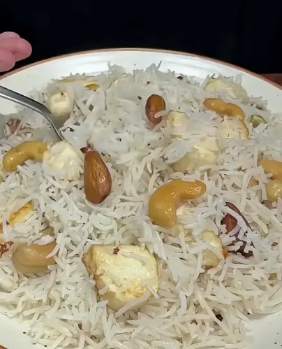 Dry fruit pulao with brown rice, cashews, raisins, figs, makhana, peanuts, and whole spices in a dark lunch container